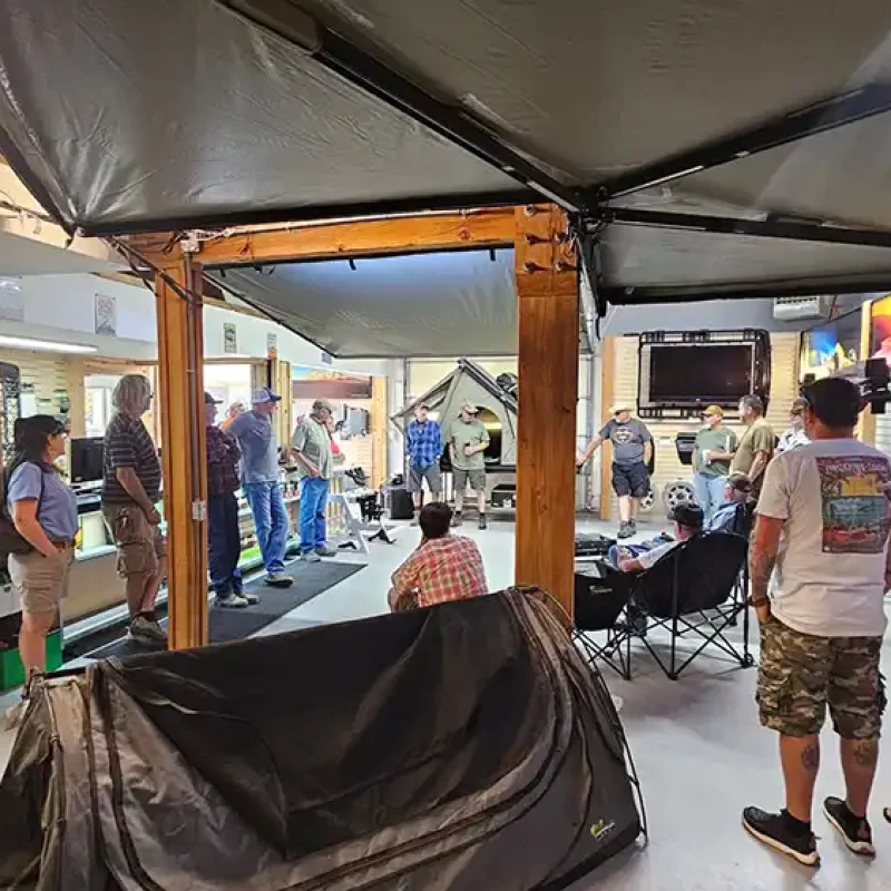 People are gathered in a store, examining a tent displayed prominently among other merchandise
